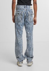Vaqueros de denim azul desgastado con costuras blancas, que presentan un ajuste holgado, grandes bolsillos traseros y un acabado lavado desvaído.