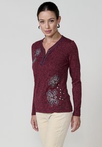 Garās piedurknēm bordo adīta krekla ar V-veida kakla izgriezumu, ar ziedu izšuvumiem un dekoratīvu šuvumu gar kakla izgriezumu. Gluda tekstūra.