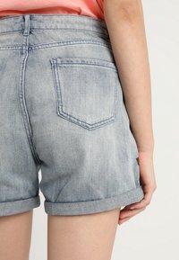 Pantalones cortos de mezclilla en azul claro con corte clásico, con dobladillo enrollado, bolsillo trasero y detalles de costura visibles.