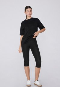 T-shirt oversize noir associé à des leggings noirs. Le tissu semble lisse, et les leggings ont une longueur mi-mollet. Baskets blanches incluses.
