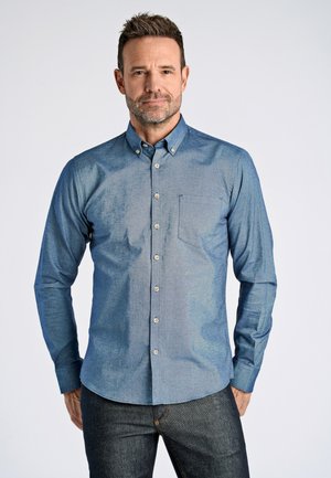 Camisa de manga larga azul clara con cuello abotonado, bolsillo en el pecho y tejido texturizado. Botones en el frente y corte entallado.