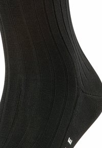 Chaussettes noires côtelées en tissu texturé, avec un renfort au talon et aux orteils, ornées de lettres blanches de la marque en bas.