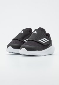 Czarne buty sportowe z teksturowaną cholewką, bez sznurowadeł, z białymi akcentami, wyposażone w gumową podeszwę i wzmocniony czubek.