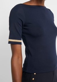 Námořnicky modrý přiléhavý top z bavlněné směsi, s detaily zlatých pruhů na rukávech a výstřihem ve tvaru lodi. Texturovaná, hladká látka.