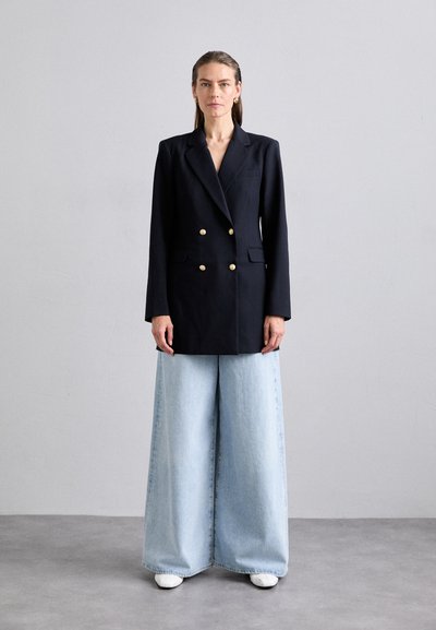 Dobbeltradet marineblå blazer med gullknapper, kombinert med vide lyseblå denimjeans. Teksturert stoff, strukturert silhuett, uformell stil.