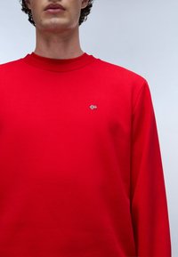 Sudadera roja hecha de tela suave, con diseño de cuello redondo, mangas largas y un pequeño logo bordado en el pecho.