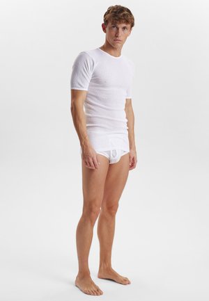 Hvid ribbet kortærmet t-shirt parret med hvide trusser, der har et tætsiddende design og glat tekstur, båret af en stående model.