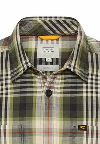 Groene, beige en zwarte geruite button-up shirt met kraag, één zwarte knop en het "Camel Active" label binnenin de kraag.