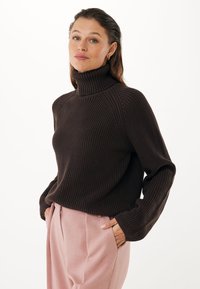 Suéter de tortuga marrón con canalé y mangas largas, combinado con pantalones rosa pálido, con un escote amplio y un ajuste relajado.