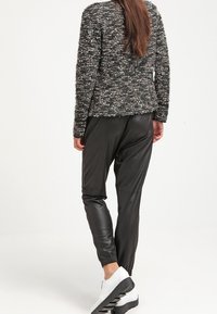 Svarta fusk läderbyxor och en strukturerad svart och grå tröja. Outfiten kompletteras av vita sportiga skor med en tjock grå sula.