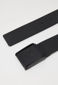 Black leather belt featuring a matte finish, rectangular metal buckle embossed with "ck," and multiple adjustment holes on the strap.