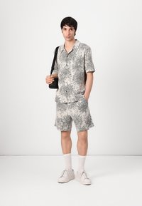 Kortermet skjorte med knapper og matchende shorts i beige med svart abstrakt mønster. Brukt med hvite sneakers og knelange sokker.
