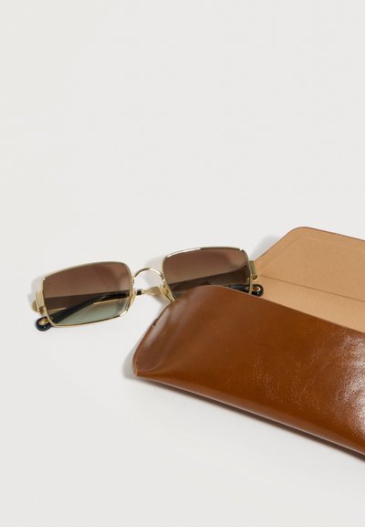 Καφέ ορθογώνια γυαλιά ηλίου με φακούς σε διαβάθμιση καφέ και χρυσά πλαίσια, που βρίσκονται εν μέρει μέσα σε καφέ δερμάτινη θήκη πάνω σε λευκή επιφάνεια.