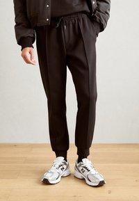 Svarta joggers med dragsko i midjan och ribbade muddar, ihop med grå och vita träningsskor med mesh-överkupper och logodetaljer.