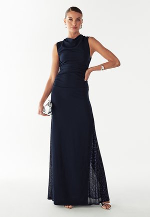 Mornarsko modra večerna obleka z izrezom v obliki kapuce, oprijetim zgornjim delom in obleko dolžine do tal. Ima stranski razporek z bleščečimi detajli s sequinom.