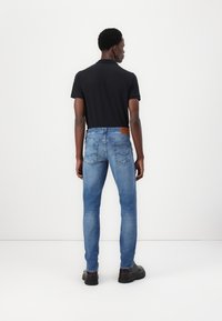 Tricou polo închis la culoare asortat cu blugi slim-fit de culoare albastru deschis, dotati cu o petec din piele maro pe talie și cu o textură netedă a denimului.