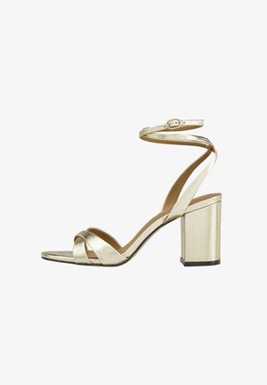 Sandale à talons hauts en métal doré avec des brides croisées à l'avant, une sangle de cheville réglable et un talon carré. Texture lisse et design à bout ouvert.