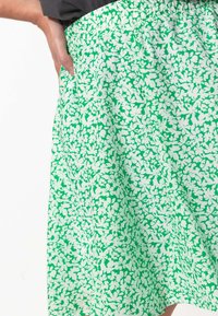 Jupe avec une taille élastique verte ornée d'un motif floral blanc. Le tissu a une texture douce et tombe dans une silhouette fluide.