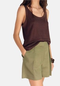 Canottiera marrone senza maniche abbinata a pantaloni corti verde chiaro con vita alta. L'outfit presenta linee pulite e una vestibilità rilassata, con tasche laterali.