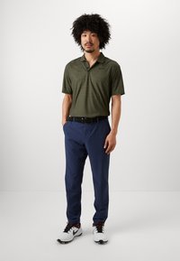 Short-sleeve, olive-green polo shirt with textured pattern, paired with navy blue trousers and white sneakers featuring black and red accents.