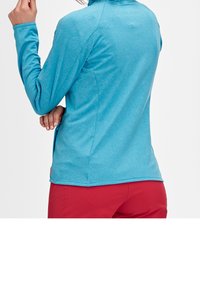 Turkusowa bluzka z długim rękawem z kołnierzykiem, o miękkiej strukturze i bocznymi rozcięciami, zestawiona z jasnopomarańczowymi spodniami. Charakteryzuje się czystym, sportowym krojem.