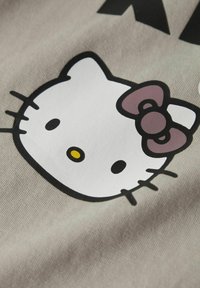 Grå fabric har et nærbillede af et tegneserie katteansigt med en pink sløjfe. Katten har sorte stænger, øjne og en gul næse.