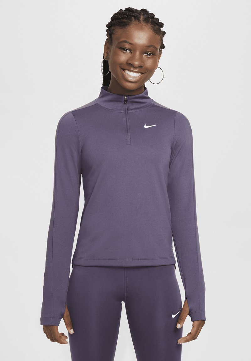 Giovane donna sorridente, veste un completo sportivo viola coordinato di Nike, composto da una felpa con zip e leggings, entrambi con il logo Swoosh bianco.