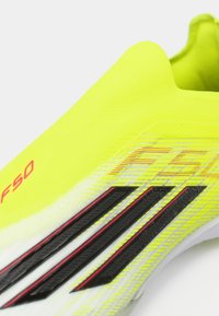 Ryškiai geltonas futbolo batai su tekstūruota paviršiumi, juodais ir raudonais akcentais bei išskirtiniu F50 prekės ženklu šone.