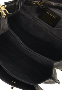 Interno di una borsa nera in pelle con due scomparti e una tasca con zip. Presenta un'imbottitura morbida e testurizzata e accessori in tonalità oro.