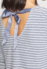 Pasiasty szary top z dekoltem na plecach, z granatowym, satynowym zapięciem w postaci kokardy. Materiał ma miękkie, teksturowane wykończenie.