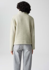 Lichtgroene gebreide trui met een hoge kraag, lange mouwen en een losvallende pasvorm, gecombineerd met lichtgrijze wijde jeans.