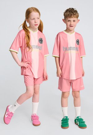 Barns fotbollskit i rosa med vertikala ränder, tillverkat av ett mjukt tyg. Har logotyp och varumärkestext. Inkluderar matchande shorts och skor.