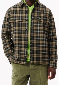 Rutig skjorta i brunt, svart och vitt med knäppning, två bröstfickor och ett grönt stickat lager underneath. Texturerad tyg.