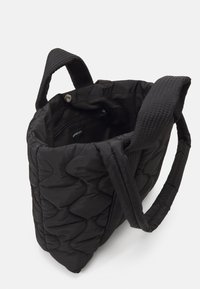 Sac cabas noir matelassé avec une texture douce, doté de deux poignées robustes, d'une poche zippée à l'intérieur et d'une fermeture à pression.