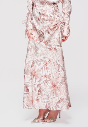 Donna che indossa un lungo abito rosa e bianco a stampa floreale con polsini annodati, abbinato a scarpe con tacchi alti, punta affilata e cinturini.