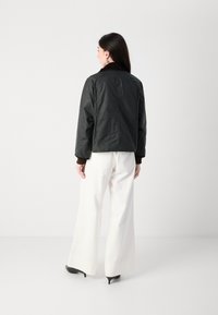 Jachetă bomber neagră cu un design scurt, cu manșete ribbed și guler maro, asortată cu pantaloni largi albi și tocuri negre.
