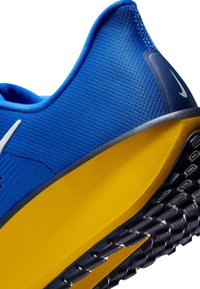 Chaussure de sport Nike présentant une tige en mesh bleu, une semelle intermédiaire en mousse jaune et une semelle extérieure en caoutchouc noir texturé avec des motifs de bande de roulement distincts.
