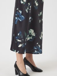 Spodnji deli noge v črnih visokih petah z temno cvetlično midi krilo, ki ima modre in bele cvetne vzorce.