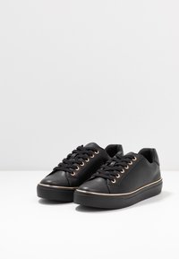 Black leather sneakers with round toe, flat rubber sole, and gold eyelets. Features laces and a stitched seam along the sole.