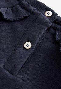 Top in cotone blu navy con colletto a costine, caratterizzato da una pattina decorata con un bottone rotondo di colore chiaro e dettagli arricciati lungo il collettino.