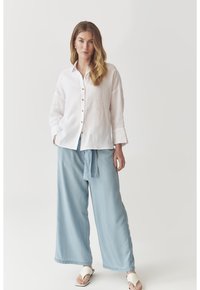 Linen button-up shirt in off-white, paired with light blue wide-leg pants. Textured fabric with a relaxed fit. White sandals complete the look.