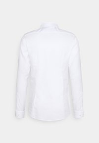 Camicia bianca a maniche lunghe realizzata in tessuto liscio, con colletto a punta e polsini con bottoni, presenta un orlo dritto. Senza motivi o dettagli.
