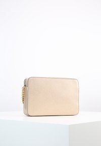Metalen gouden rechthoekige clutch met een gladde textuur, ritssluiting en een kettingband aan de zijkant. Eenvoudig ontwerp met subtiele stiksels.