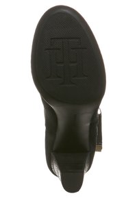 Czarna podeszwa buta na obcasie z teksturowanym bieżnikiem, lekko spiczastym kształtem i wytłoczonym logo, charakteryzująca się subtelnym połyskiem i gładkim wykończeniem.