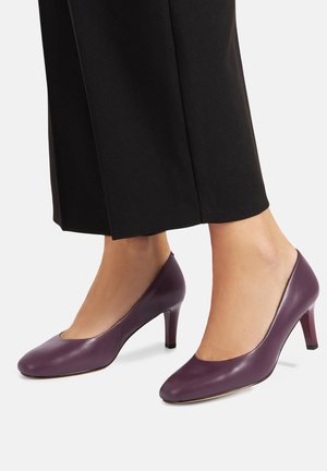 Fioletowe skórzane buty na wysokim obcasie z zaokrąglonym noskiem i małym ozdobnym wycięciem. Posiadają 7 cm obcas, gładką fakturę i minimalistyczny design.