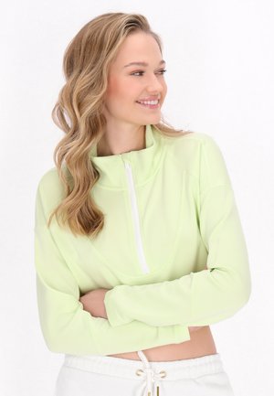 Lys grøn zip-up sweater med høj krave, tætsiddende design og lange ærmer. Glat tekstur med frontlynlås, der er parret med hvide bukser.