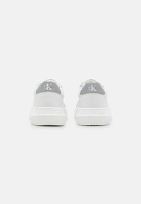 Bílé tenisky s texturovanou gumovou podrážkou a šedými akcenty na patě. Na zadní straně a jazyku se nachází logo Calvin Klein.