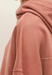 Sweat à capuche surdimensionné en tissu rose doux, doté d'une grande capuche, de détails de couture subtils et d'une silhouette décontractée.