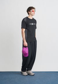 Μαύρο T-shirt με γκρι λεπτομέρειες και λογότυπο «NIKE SHOX», συνδυασμένο με μαύρο παντελόνι, γκρι αθλητικά παπούτσια και σκισμένο μωβ καπέλο.