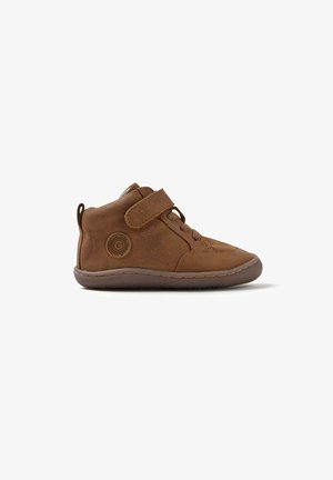 Botas de cuero marrón hasta el tobillo con una correa de Velcro, suela de goma plana y detalles de costura; diseñadas para la comodidad y facilidad de uso.